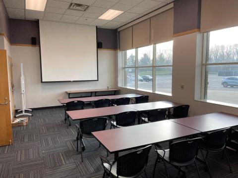 Empty room with maroon tables in two rows and a projector screen.